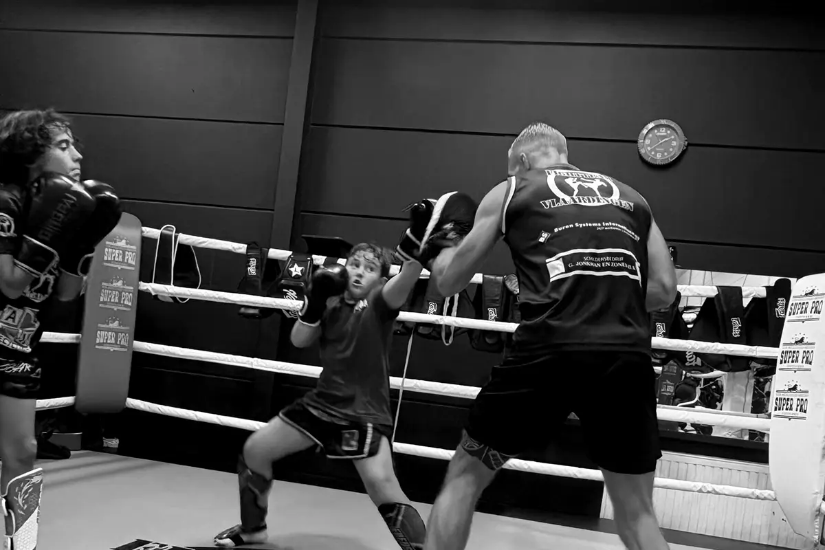 Een trainer houdt de pads vast voor een jeugdlid in de ring van Fightteam Vlaardingen